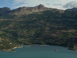 AERIAL Village near shore of Lac de Serre-Poncon with boats in water and traffic on road/ Alpes-Maritimes, France Stock Footage