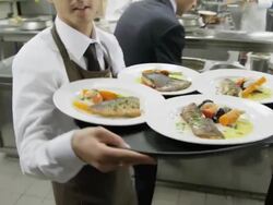 POV waiter taking prepared plates from the plating area in a restaurant kitchen to carry them to the dining room; camera precedes waiter into dining room Stock Footage