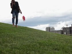 MS Young girl walking through grassy field in urban park carrying flowers and smiling while talking on her cell phone / Minneapolis, Minnesota, United States Stock Footage