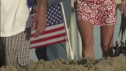 Pedestrians pass a small American flag that waves from a pile of dirt. Stock Footage