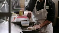 Chef sprinkles salt over raw steak in busy restaurant kitchen Stock Footage