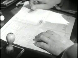 A hand uses a rubber stamp on a document. News Clip