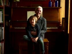 Slow push in on portrait of grandmother and grandson sitting on a piano bench, looking into the camera. Stock Footage