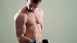 beautiful athlete trains with a dumbbell on a grey background Stock Footage