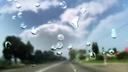Raindrops splash and trickle down a windshield as a vehicle drives along a highway. Stock Footage
