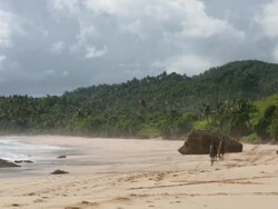 Two boys on horseback galloping towards camera across windswept beach with green hills in background Stock Footage