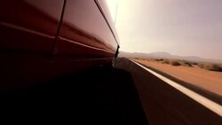 A red vintage convertible drives close to the solid white line at the edge of a desert highway. Stock Footage