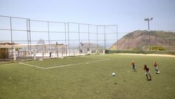 Young Brazilian boys chase soccer ball across turf field overlooking Rio de Janeiro Stock Footage