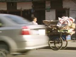 WS View of man transporting scrap paper and cardboard through city by tricycle with passing vehicles on streets / Shanghai, China Stock Footage