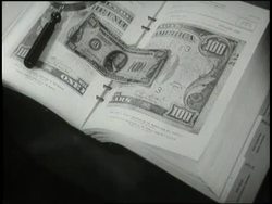 A man uses a magnifying glass to compare counterfeit money to photographs of bills in a book. News Clip