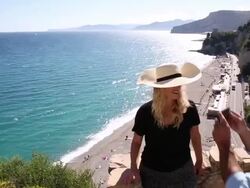 Man takes pic of woman on stone wall above beach Stock Footage
