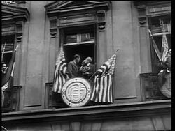 B/W 1927 low angle long shot Charles Lindbergh holding US flag standing on balcony with French officials / Paris Stock Footage
