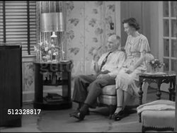 1952: HOME LIFESTYLE:  MS Male & female (middle aged, 40's or 50's) sitting in living room watching television (not in frame), male smoking pipe, talking to female. Married, marriage, family, husband & wife, couple, domestic Instructional Video