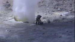 A volcanologist carries testing equipment to the edge of a smoking volcano. Stock Footage