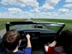 WS Young couple in convertible woman taking photo of man with digital camera while driving on rural road through grain fields/Washington, USA  Stock Footage