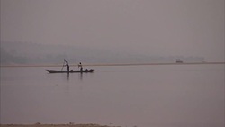 Long shot of two fishermen paddling down river on a boat Stock Footage