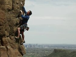 Man climbs a steep rock  facewith the city of Denver in the background Stock Footage