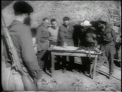 B/W 1959 guerrilla soldier watches as Fidel Castro points to map on table surrounded by men / news. Stock Footage