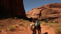 Follow hikers on desert path surrounded by rocky mountains in Utah (tilt down) Stock Footage