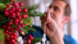 Father and son reach to hang ornaments on Christmas tree Stock Footage