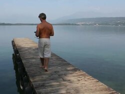 Pan down as man walks along lake pier, with digital tablet Stock Footage