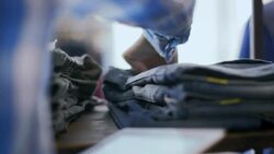 Young employee counts pants on shelf and types data on tablet in modern clothing store Stock Footage