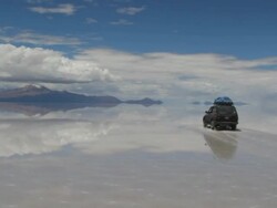 Car crossing the vast salt desert covered with a mirror like film of water after rain. Bolivia, Salar de Uyuni Stock Footage