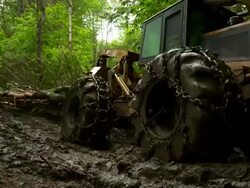 Full shot of skidder as it drags trees through the mud, moving screen right, moving toward the camera, then away from the camera. Stock Footage