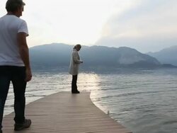 Woman feeds swan at lake pier, is joined by man Stock Footage