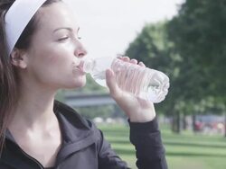 CU Shot of young female jogger relaxing at city park after her jog and drinking water in bottle / Portland, Oregon, United States  Stock Footage