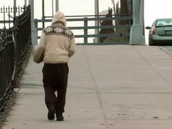 Man in a long sleeve hoody walking down a side walk near a fence in the bronx dribbling a basketball during the day Stock Footage