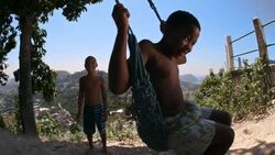 Brazilian boy on swing smiles at camera as friend watches and waits his turn Stock Footage