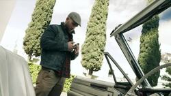 Young man texts on smartphone, gets in convertible and turns key in ignition Stock Footage