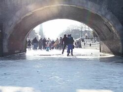Ice Skating On Frozen Amsterdam Canal under a Bridge Stock Footage