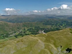 Aerial view over summit of Lingmoor Fell in the Lake District to reveal village of Chapel Stile in the valley below / Cumbria, England Stock Footage