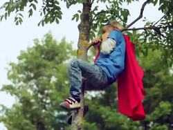 Little boy-superman climbs on a tree. Stock Footage