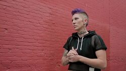 Cool tough young woman with purple hair and tattoos looking away in urban alley Stock Footage