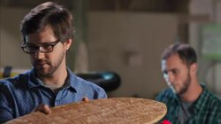 Young craftsman holds up and inspects wooden longboard in busy skate shop Stock Footage