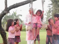 Senior man swinging her granddaughter at holi festival  Stock Footage