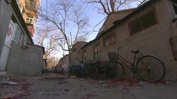Trash blows through an alley where a bicycle and ramshackle furniture lean against a house. Stock Footage