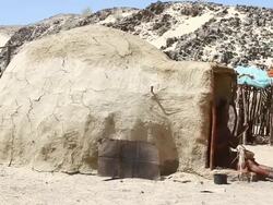MS Native himba woman sitting down in front of clay hut weaving basket / Himba, Kunene, Namibia Stock Footage