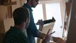 Shop workers box up skateboard for shipment, talk on smartphone and manage account on laptop Stock Footage