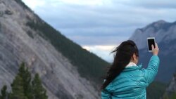 Pan to woman taking smart phone pics of mountain scene Stock Footage
