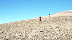 Mountain bikers descend steep mountain slope, from summit Stock Footage