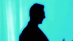 A man in silhouette standing against a blue background gestures with his hands as he speaks. Stock Footage