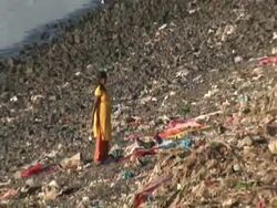 Woman on banks of river sifting through rubbish, zoom out to city, Mumbai, India Stock Footage