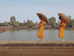 MS Buddhist monks walk along the edge of a moat with Angkor Wat temple in the background, carrying parasols / Siem Reap, Cambodia Stock Footage