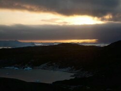 WS T/L View of clouds moving through sky at sunset as sun sets with mountains and icebergs below / Ilulissat, Greenland Stock Footage