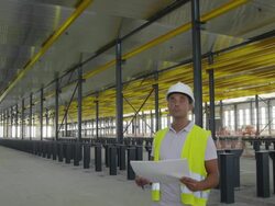 WS engineer holding plan standing in large hangar, looking around ostensible checking things, front view, RED R3D 4K Stock Footage