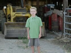 Slow motion push of boy with cleft lip standing in front of tractor. Stock Footage